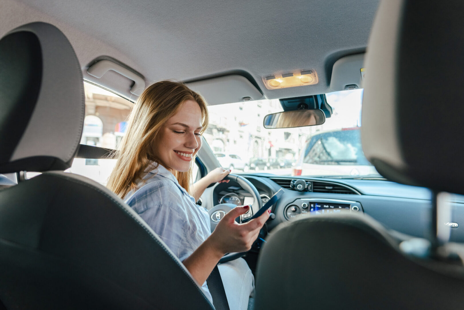 Smiling woman driver glances back holding phone