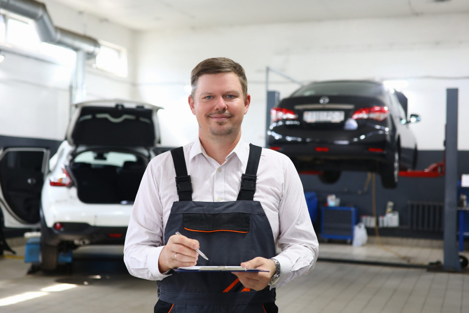 Young professional auto mechanic holding clipboard with pen. Auto insurance and car service concept